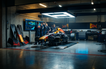 Red Bull Racing engineers reviewing aerodynamic data on a monitor inside the team's technical facility, with the RB21 Formula 1 car partially disassembled in the background.