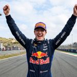 Palmowski Wins Zandvoort Feature Race, Extends Championship Lead Photorealistic image of a female Red Bull racing driver smiling joyfully and celebrating with both arms raised in victory at the Circuit Zandvoort Formula 1 track, wearing her blue racing suit and cap.