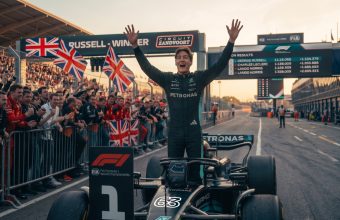 Photorealistic image of Formula 1 driver George Russell celebrating a victory on the Zandvoort circuit, standing with arms raised. Fans with Union Jack flags, Mercedes, and Ferrari apparel cheer behind him. A screen displays the podium: 1. George Russell, 2. Charles Leclerc, 3. Lando Norris.