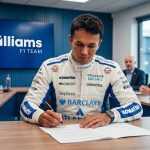 A detailed photo of Formula 1 driver Alex Albon, in full Williams Racing race suit featuring multiple sponsor logos (like Duracell, Komatsu, and Gulf), seated at a desk in a modern boardroom. He is intently focused on signing a contract document with a pen. In the background, a large screen clearly displays the white 'Williams F1 TEAM' logo on a blue background, and several other individuals in suits are seated, out of focus, around the desk.