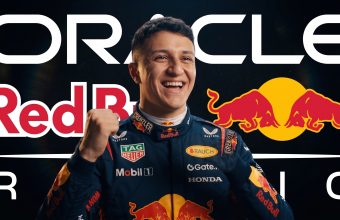A smiling Red Bull Racing driver in a racing suit with sponsor logos, raising a fist in celebration, against a background that includes text for Oracle, Red Bull, and the team logos.