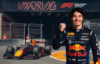 "Portrait of smiling Bulgarian F2 driver Nikola Tsolov in his Red Bull suit, fist raised, standing near his #12 F2 car at the IFEMA Madrid street circuit."