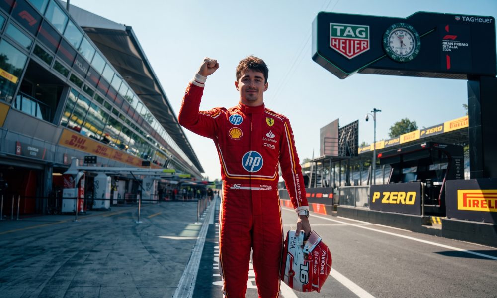 "Charles Leclerc stands on the Monza F1 track pit straight, holding his helmet in his left hand and raising his right fist in celebration after the Italian Grand Prix."