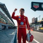 "Charles Leclerc stands on the Monza F1 track pit straight, holding his helmet in his left hand and raising his right fist in celebration after the Italian Grand Prix."