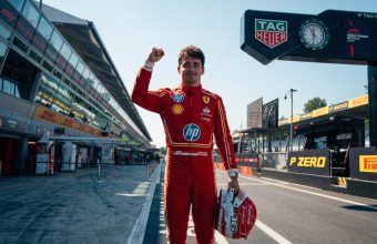 "Charles Leclerc stands on the Monza F1 track pit straight, holding his helmet in his left hand and raising his right fist in celebration after the Italian Grand Prix."